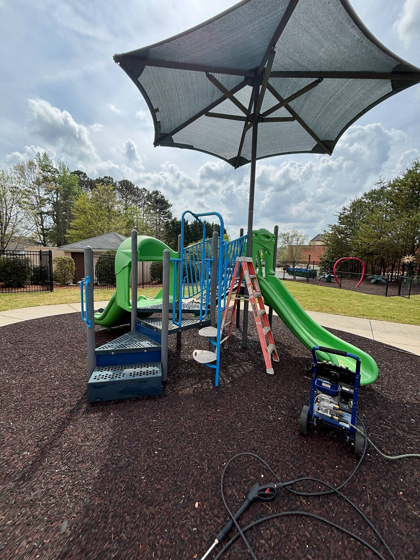 Colorful playground with slides and climbing structure under a large shade canopy on a rubber play surface