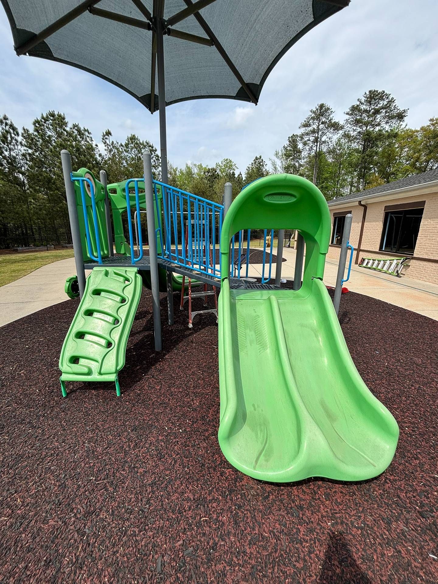 Green playground slide with stairs under a large shade canopy in a park setting