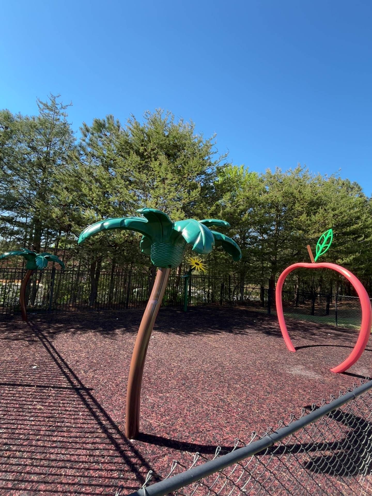 Playground with colorful leaf-shaped climbing arches under a clear blue sky, viewed behind a fence.