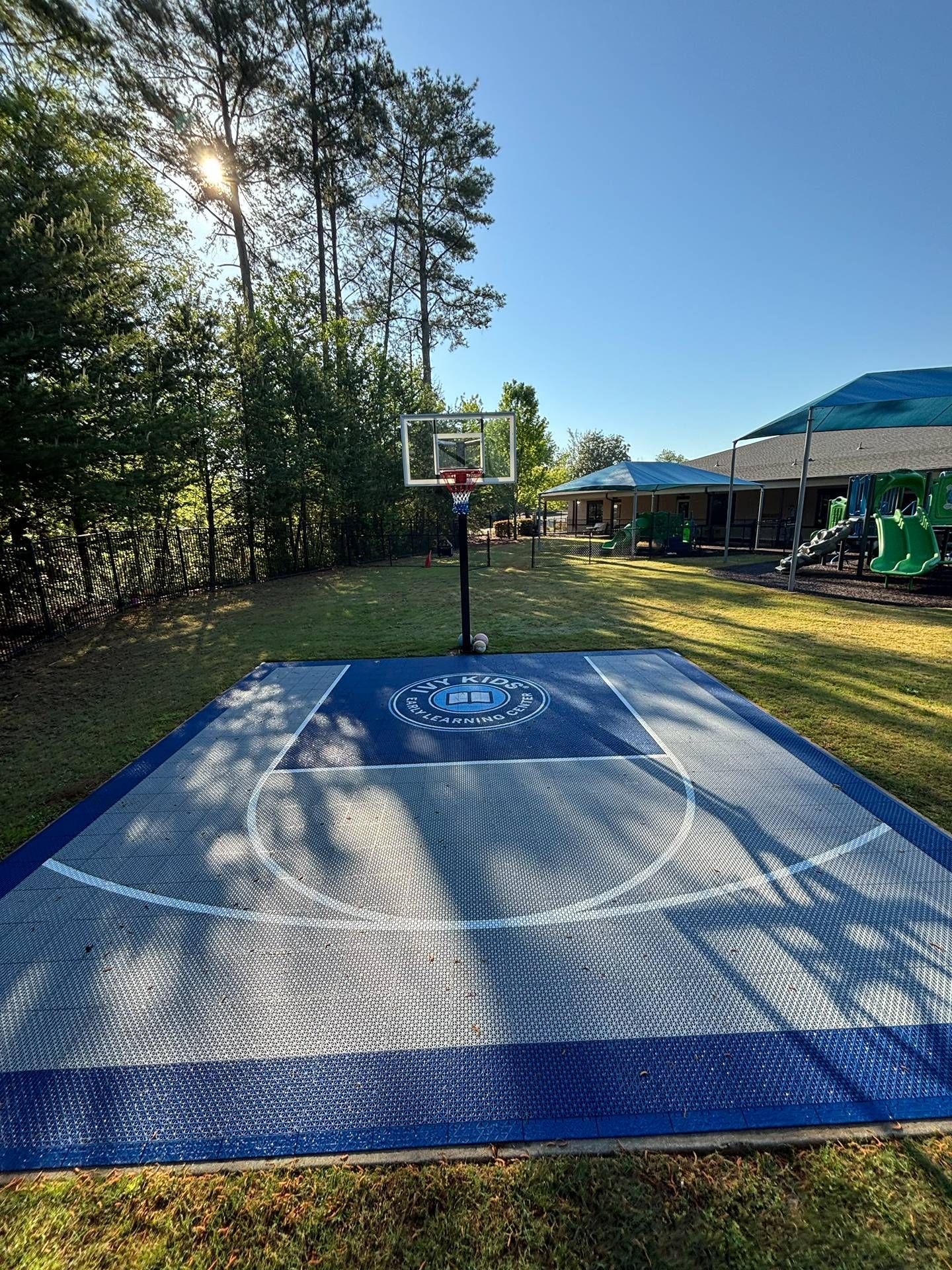 Backyard basketball hoop on a blue outdoor court, with trees and a house in the background.