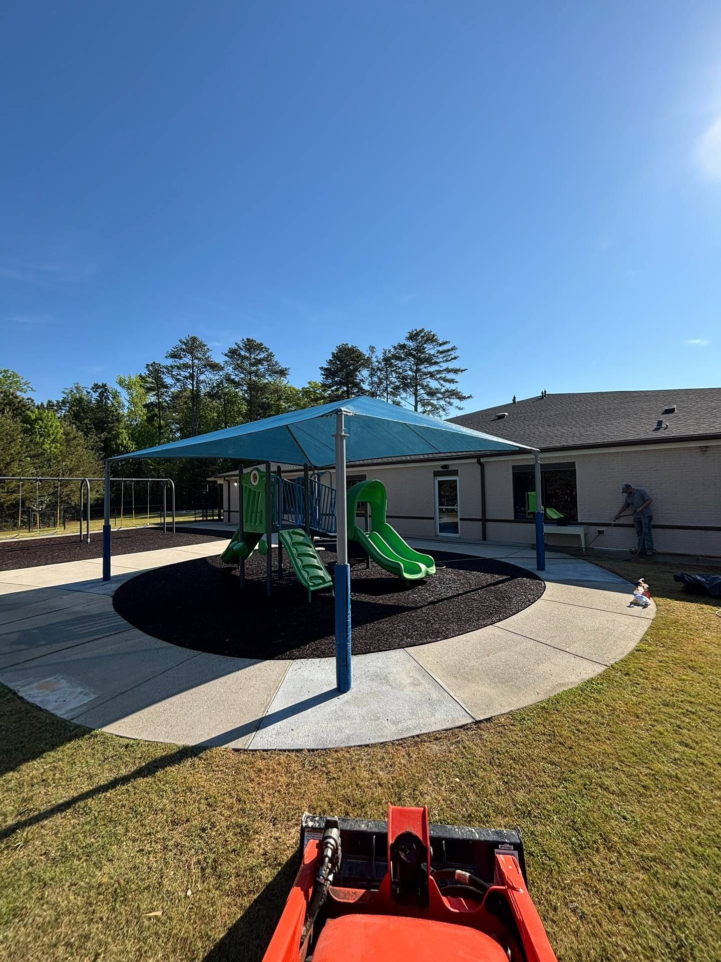 Backyard playground with blue canopy, green slide, and small red toy on grass under a sunny sky
