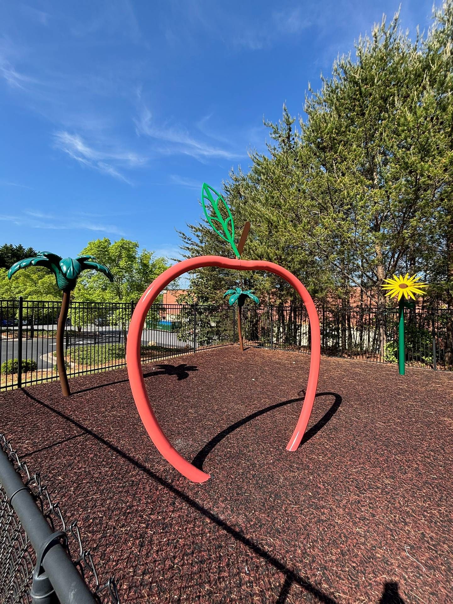 Red hoop obstacle in a playground with wood chips, trees, and blue sky