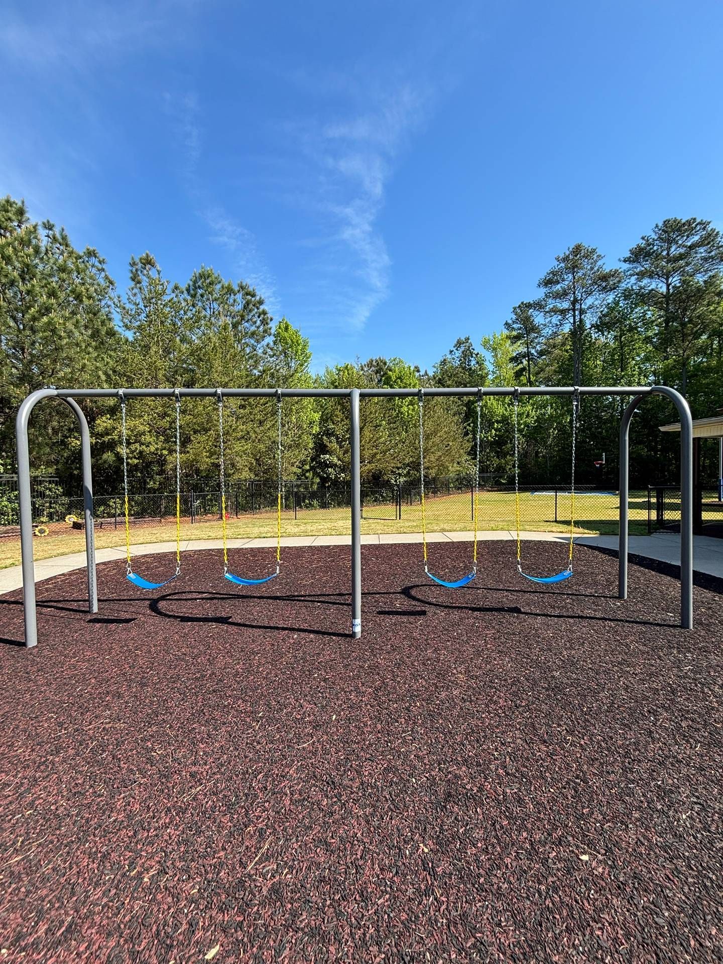 Outdoor playground swing set on wood-chip ground with blue seats under a clear blue sky