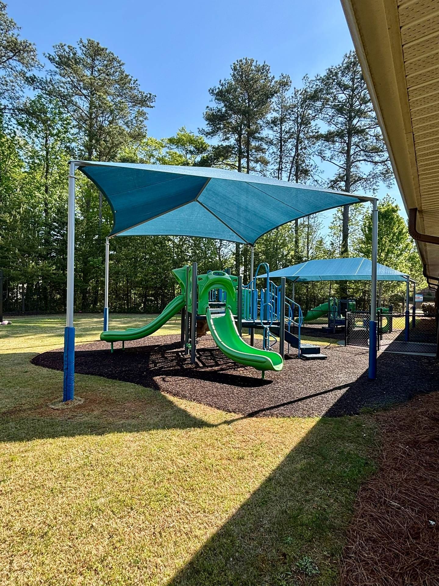 Playground with green slides under blue shade sails in a sunny park