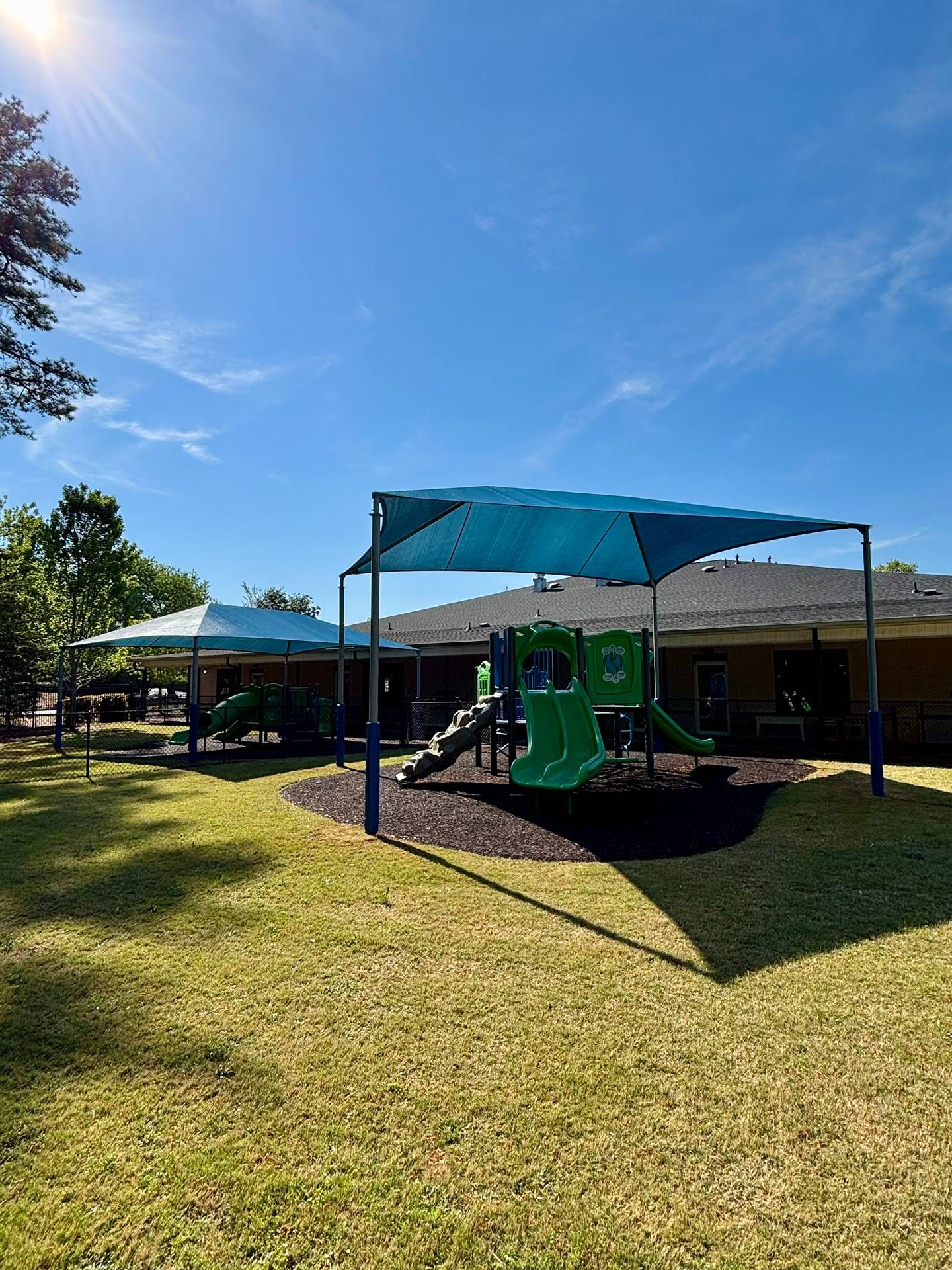 Playground with green slide and blue shade canopy on a sunny grassy field