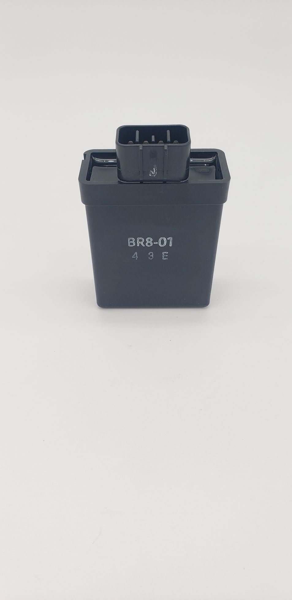 Black electronic device with a connector on top, sitting on a white surface.