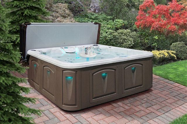 A hot tub is sitting on a brick patio in a garden.