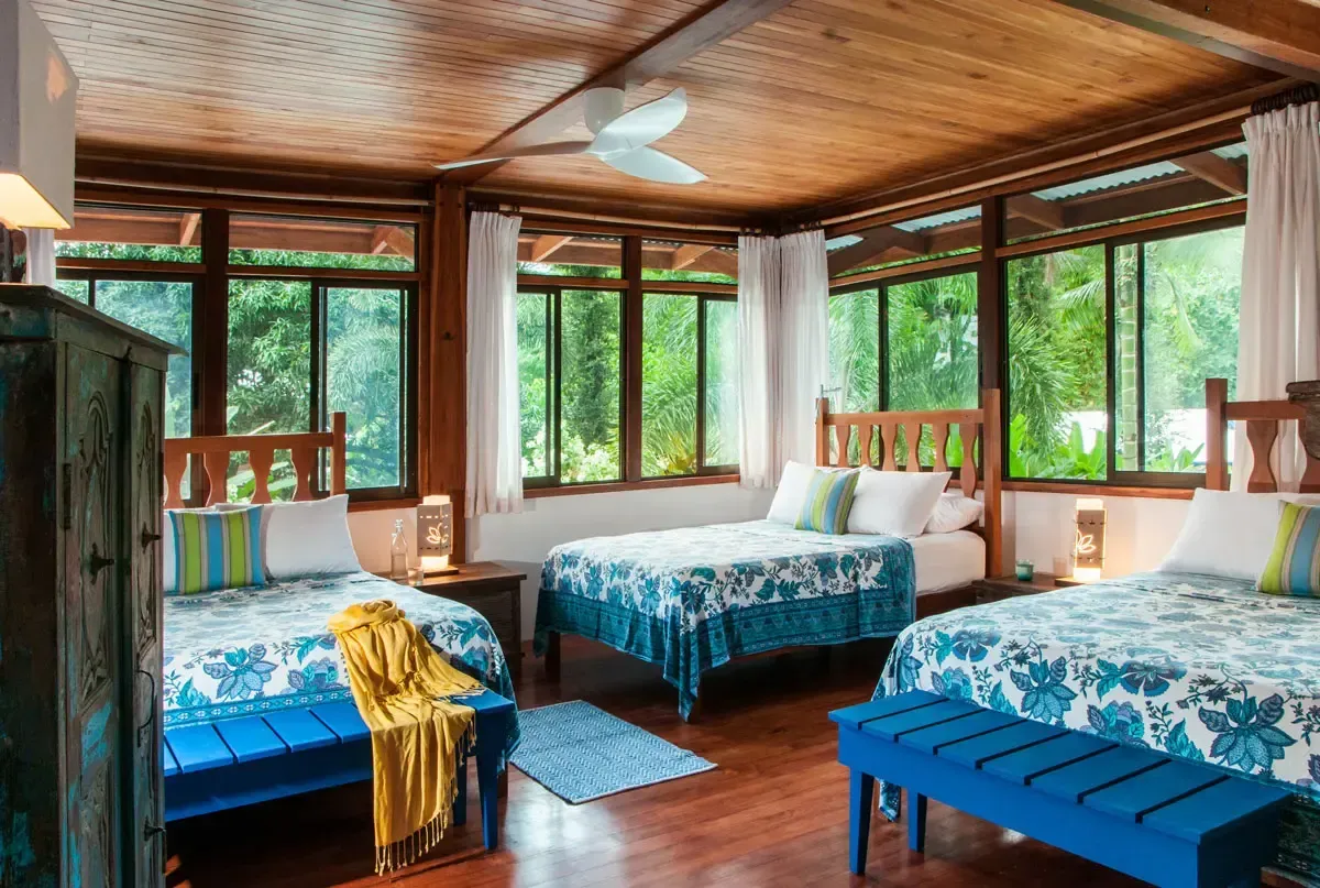 Two twin beds with white linens and patterned throws in a room with wood-paneled walls and a window.