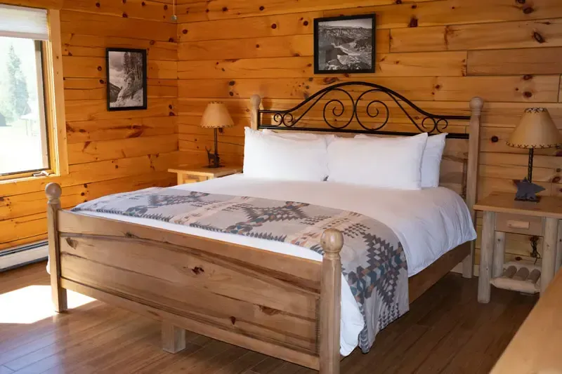 A rustic bedroom with wood-paneled walls, a wooden bed frame, patterned bedding, and two bedside lamps.