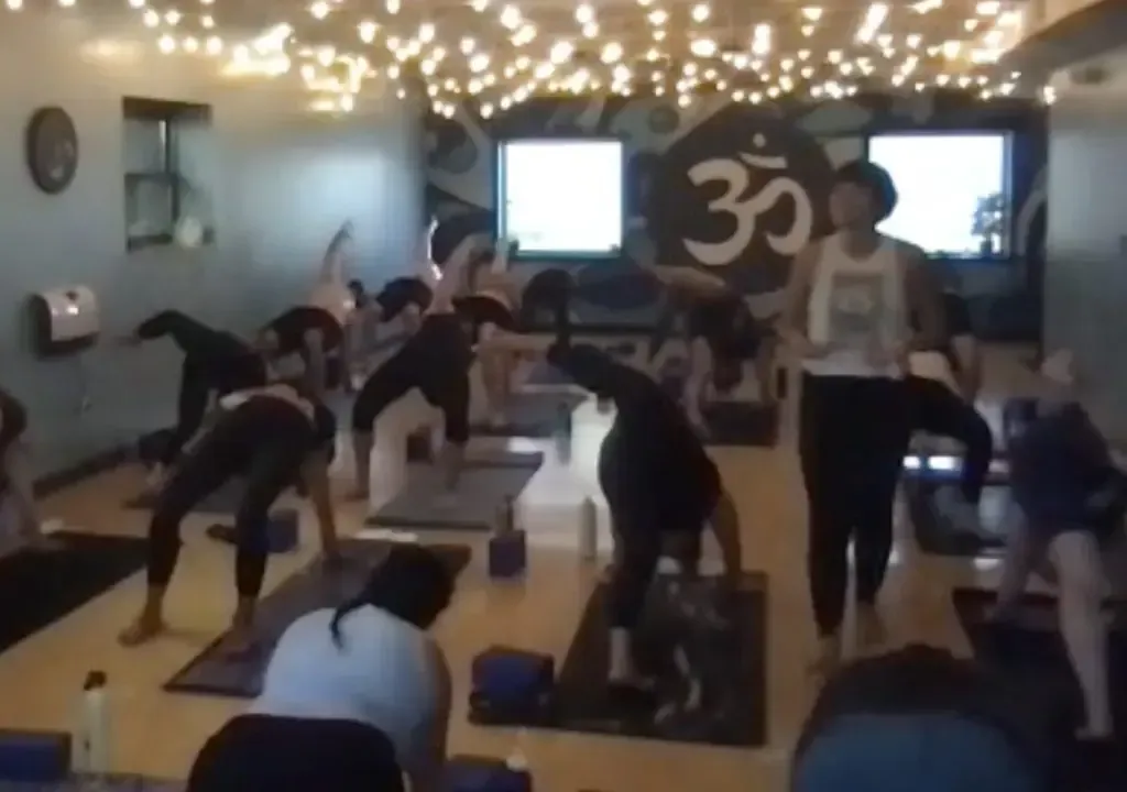 A group of people in a yoga studio performing balancing poses with an instructor standing nearby.