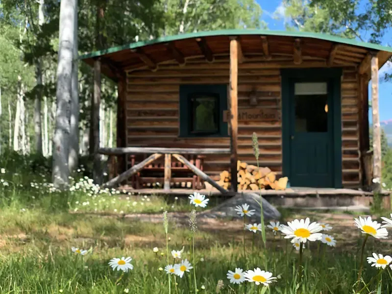 A rustic log cabin with a covered porch sits in a clearing surrounded by aspen trees.