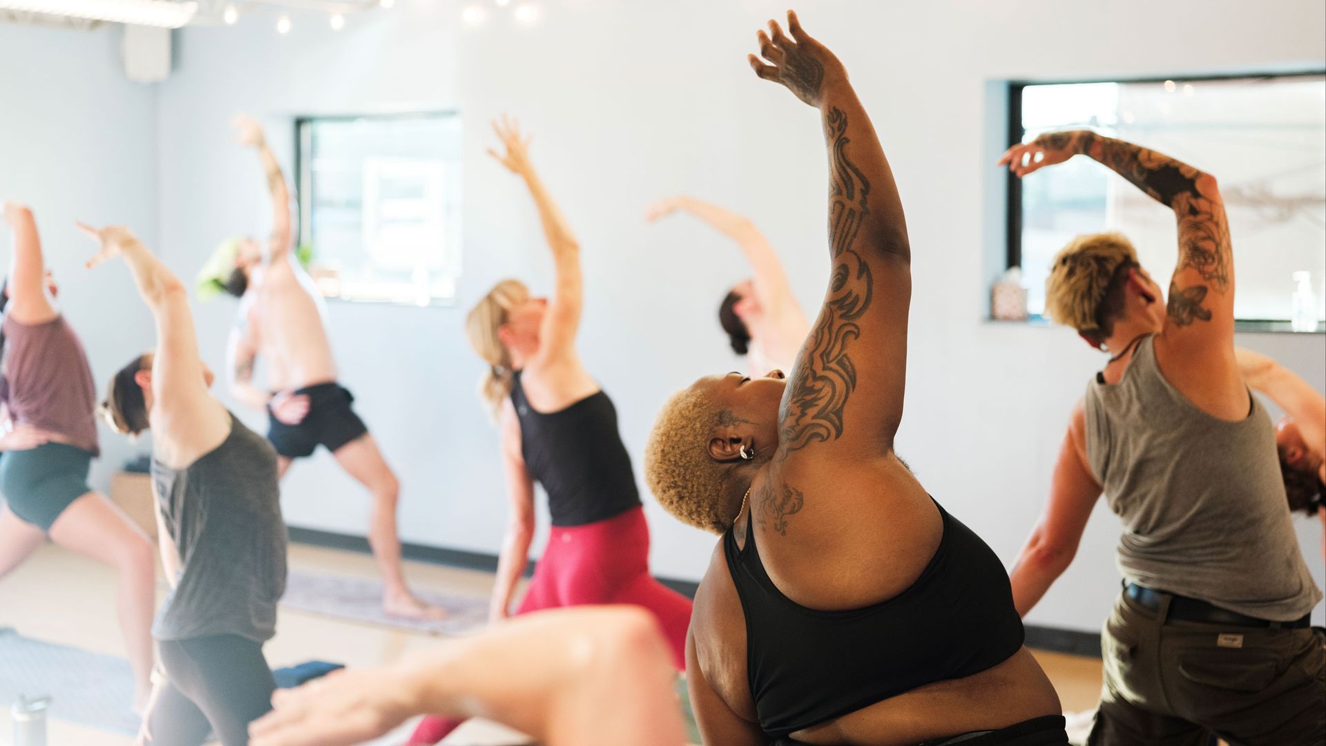 People in a yoga class stretching arms overhead in a bright studio