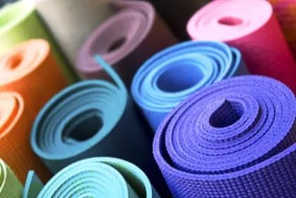 A high-angle view of multiple yoga mats in various colors, including purple, blue, orange, and light green, rolled up.