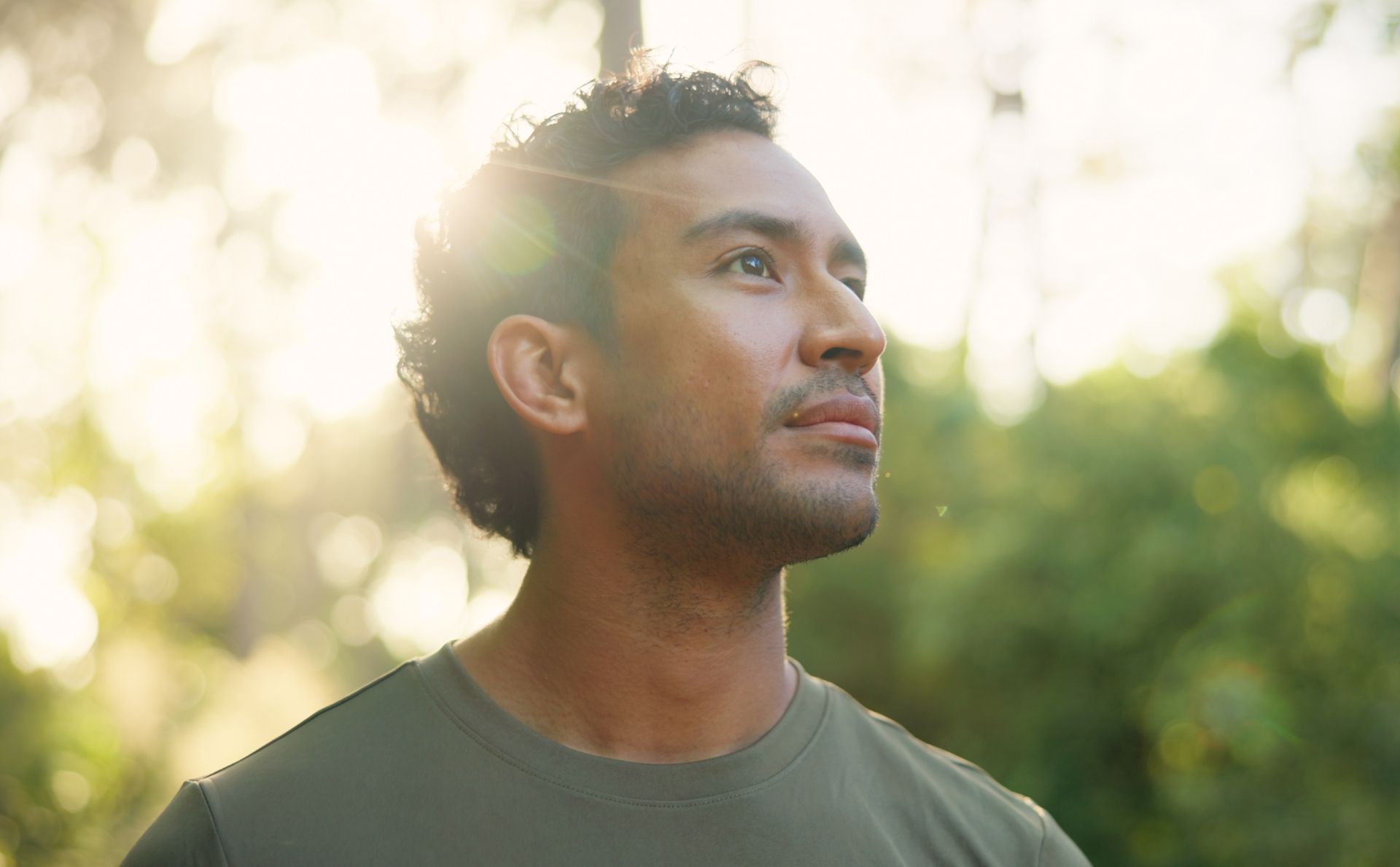 Man standing outdoors in warm sunlight, looking upward with a calm expression.