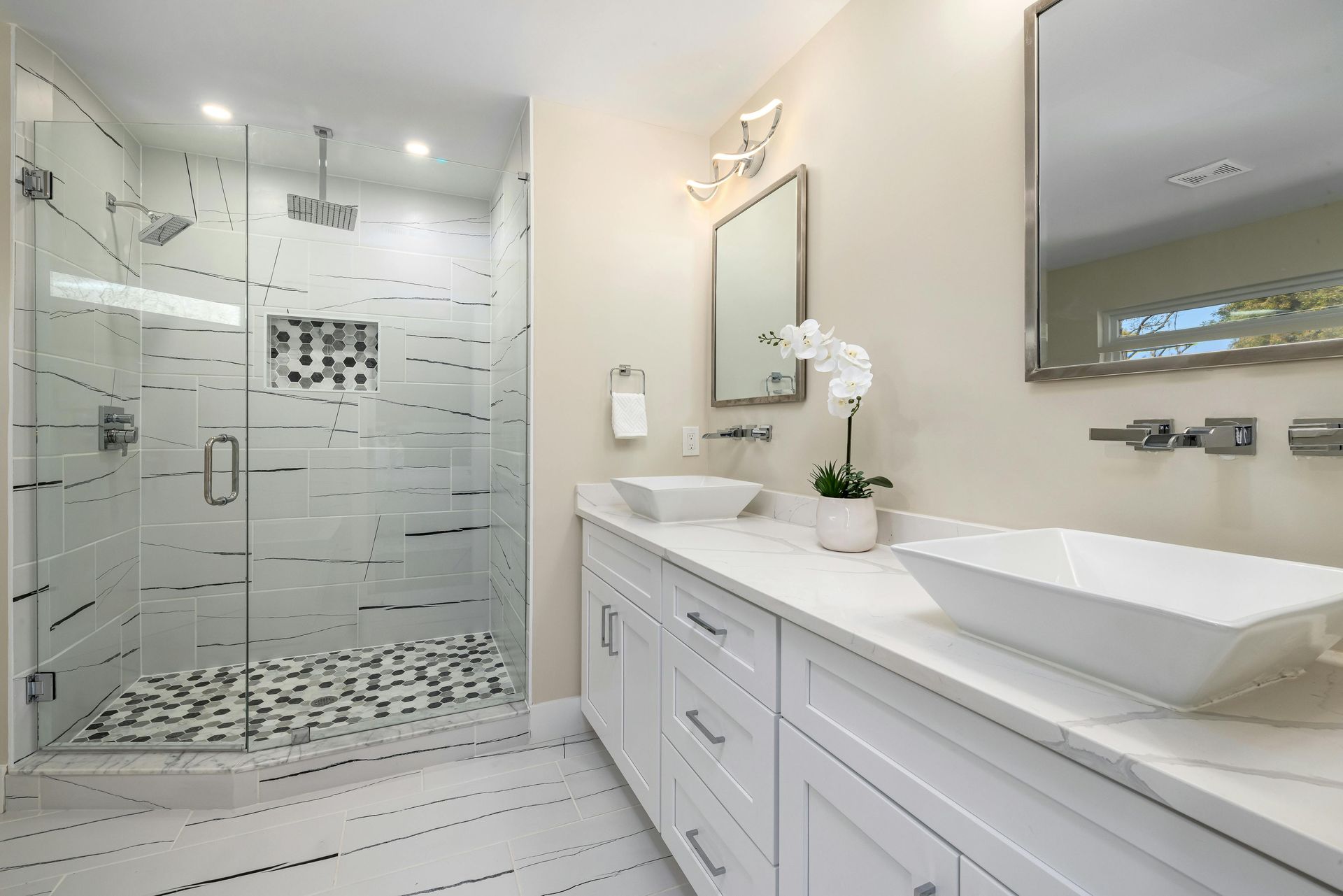 A bathroom with two sinks , a walk in shower and a mirror.