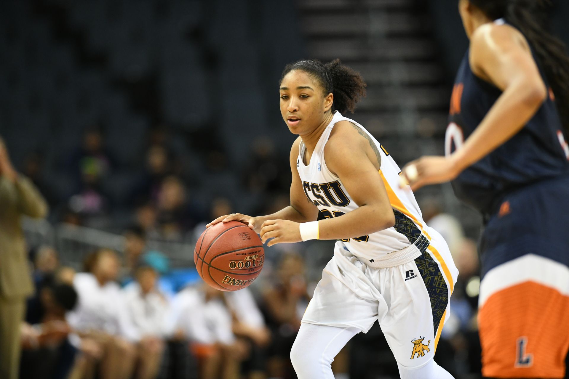 Basketball player in white dribbles on court during a game, with defenders nearby.