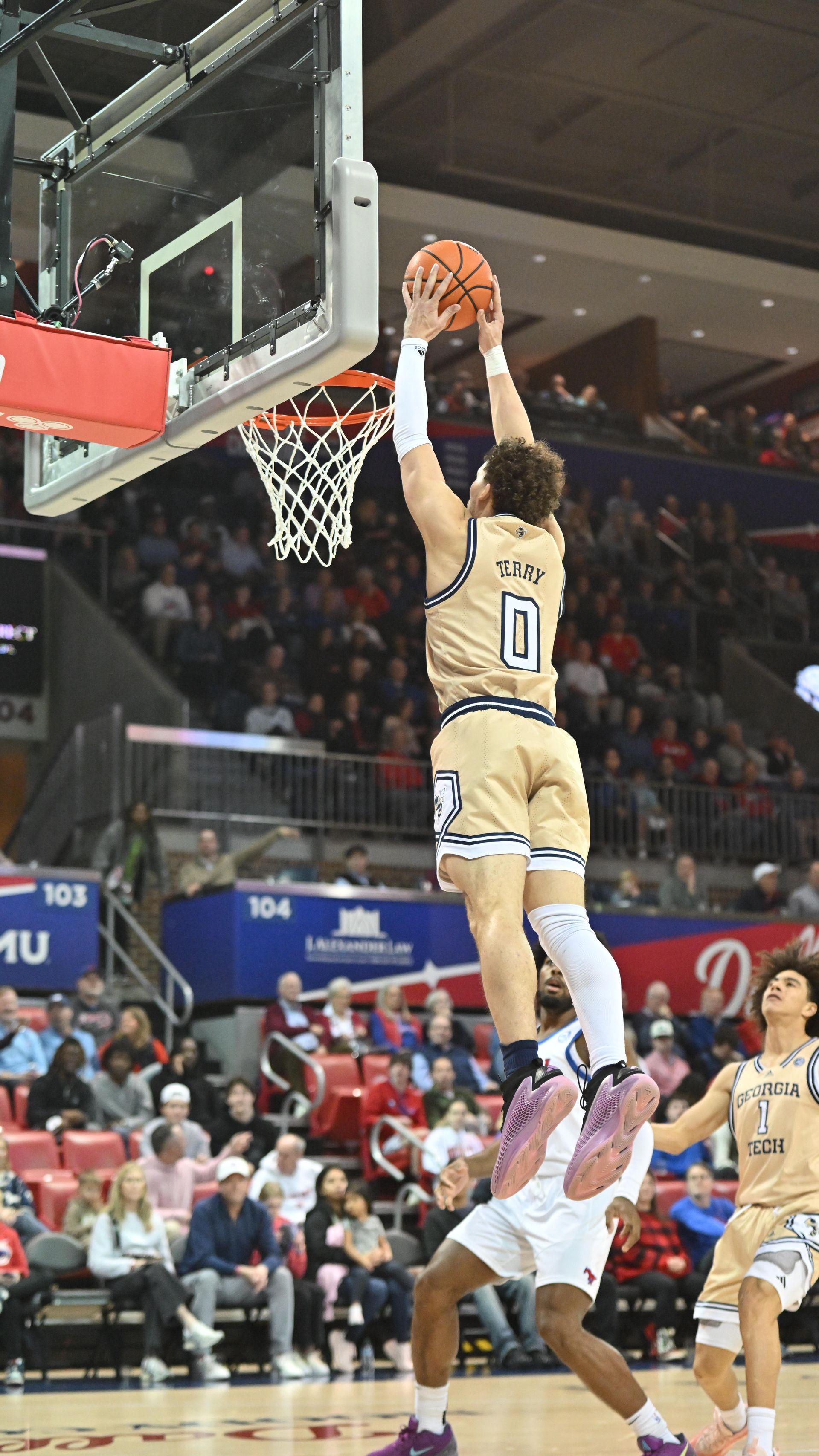 Basketball player in gold jersey leaps for a two-handed dunk near the hoop during a game