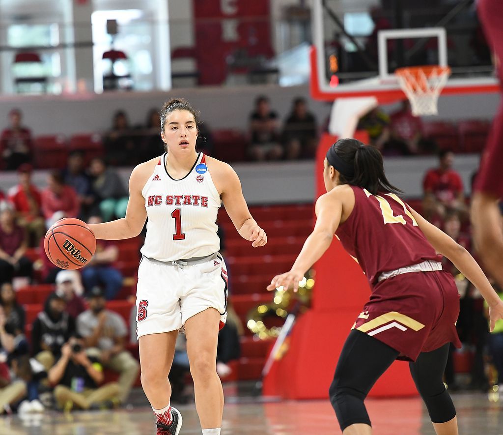 Women’s basketball game: white-uniformed player dribbles past maroon-uniformed defender.