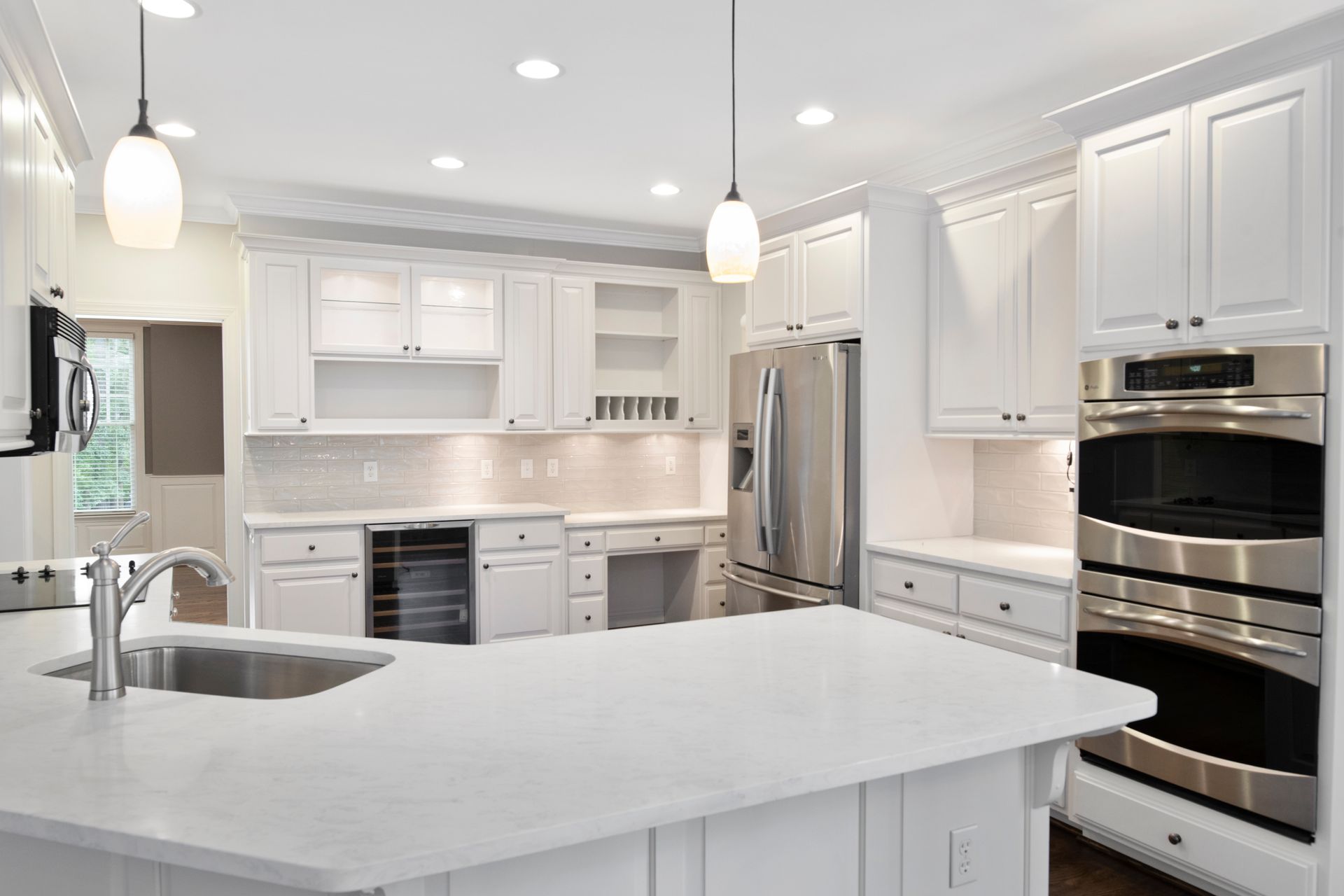 Bright white modern kitchen with island, stainless steel appliances, and pendant lights