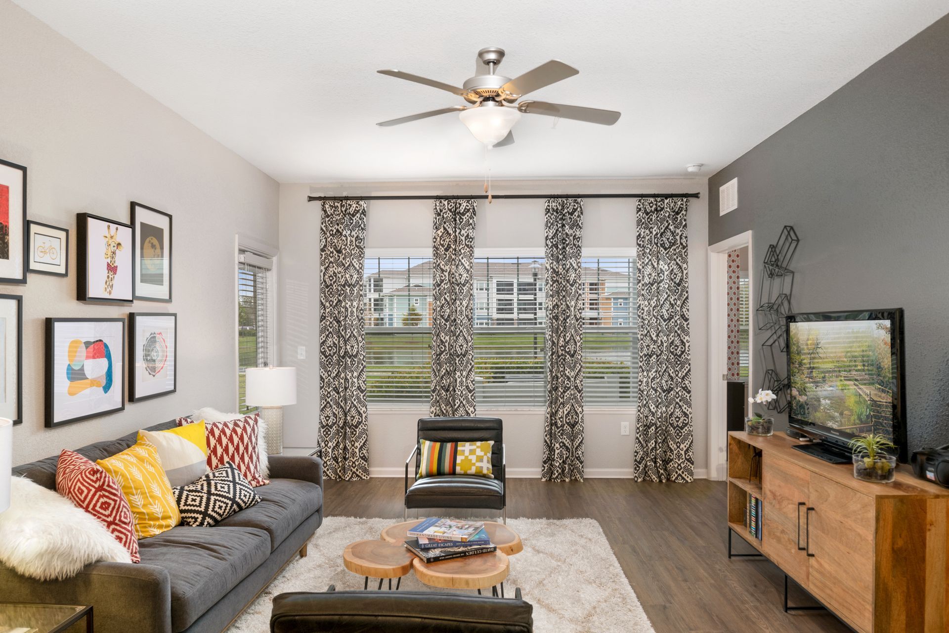 Modern living room with gray sofa, patterned curtains, wooden TV stand, and ceiling fan