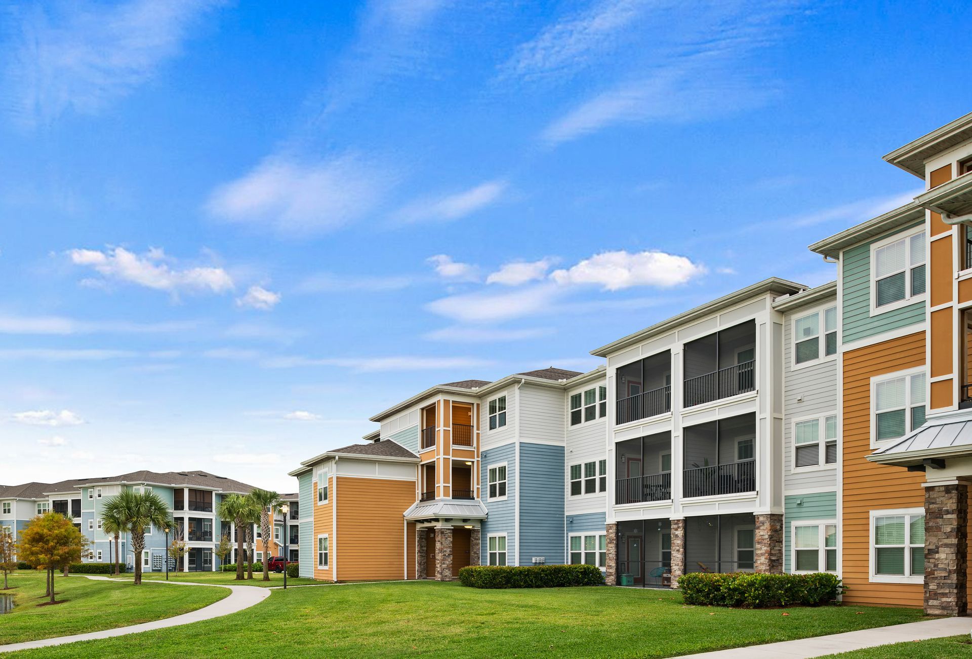 Modern apartment complex with balconies, green lawn, and blue sky