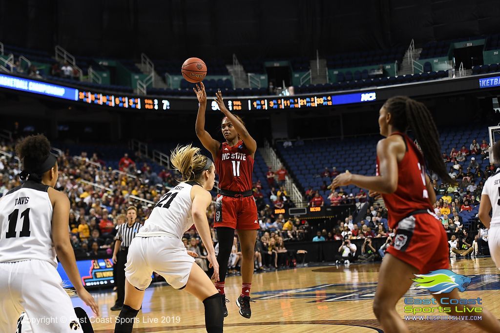 Basketball player in red shoots over defenders in a crowded indoor arena