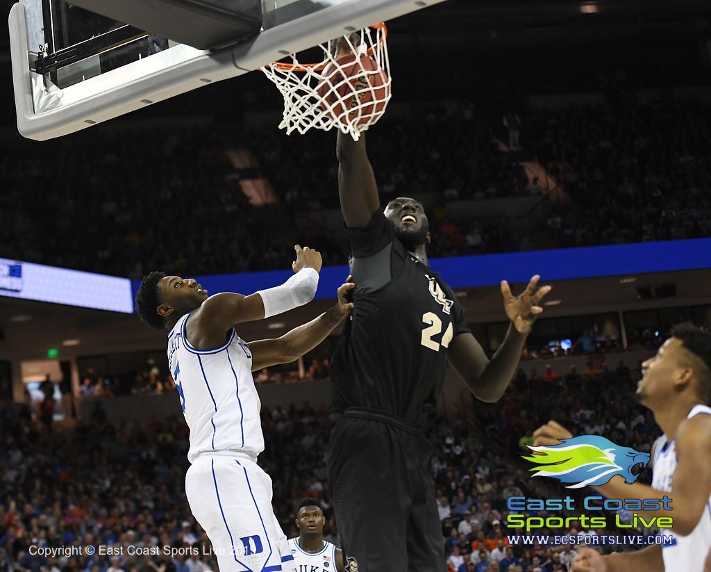 Basketball player in black attempts a shot at the hoop as a defender in white contests in a packed arena