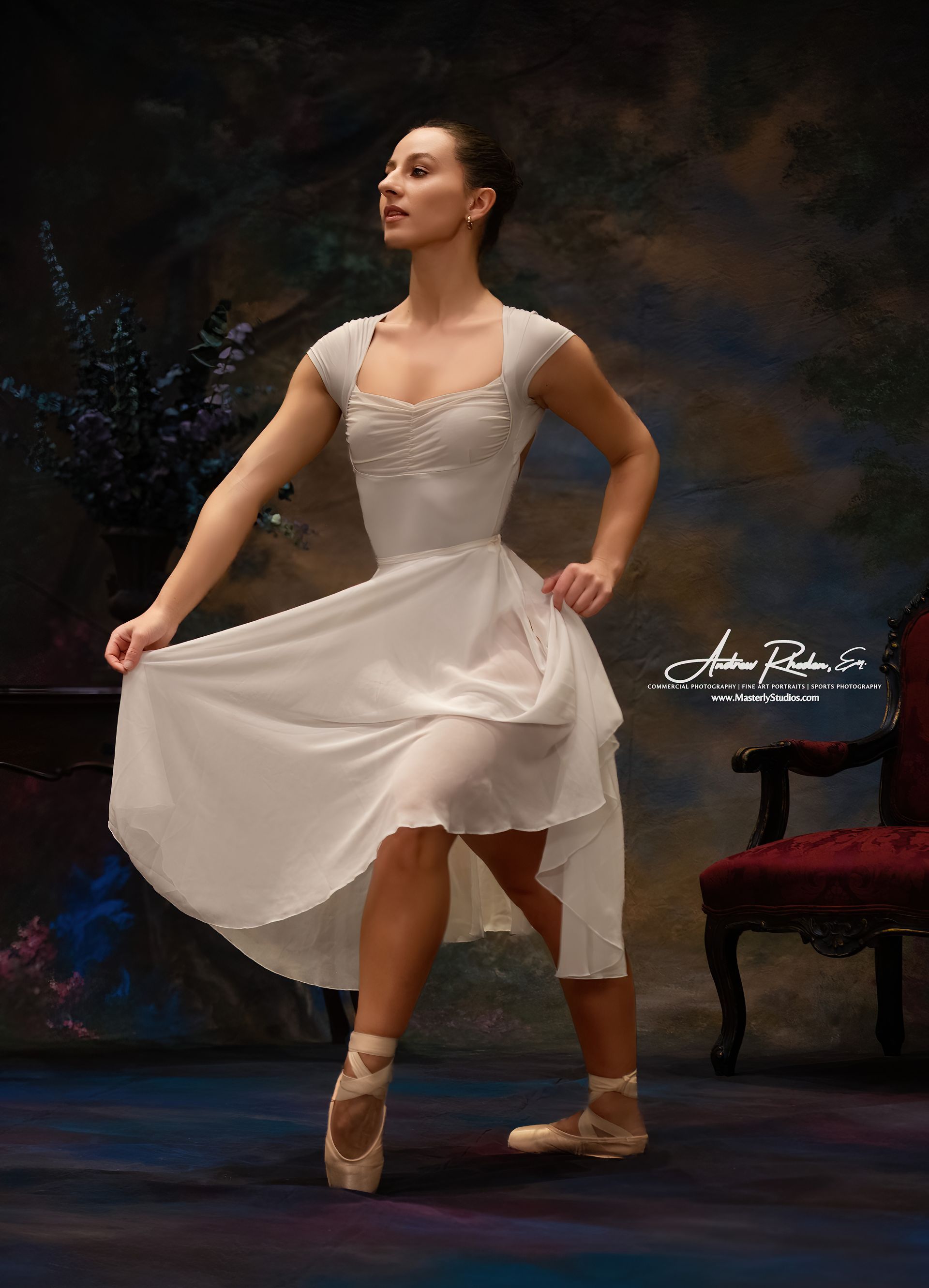 Ballet dancer in white dress and pointe shoes posing on stage, with a chair in the background