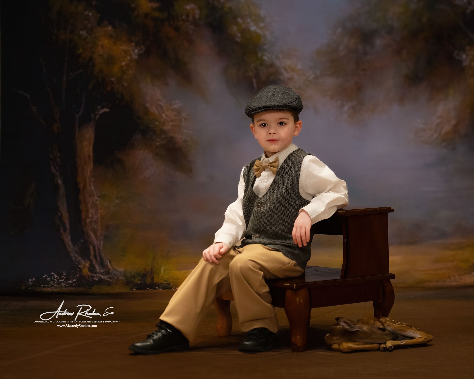 Child seated on a wooden bench in vintage attire with flat cap, against a painted studio backdrop