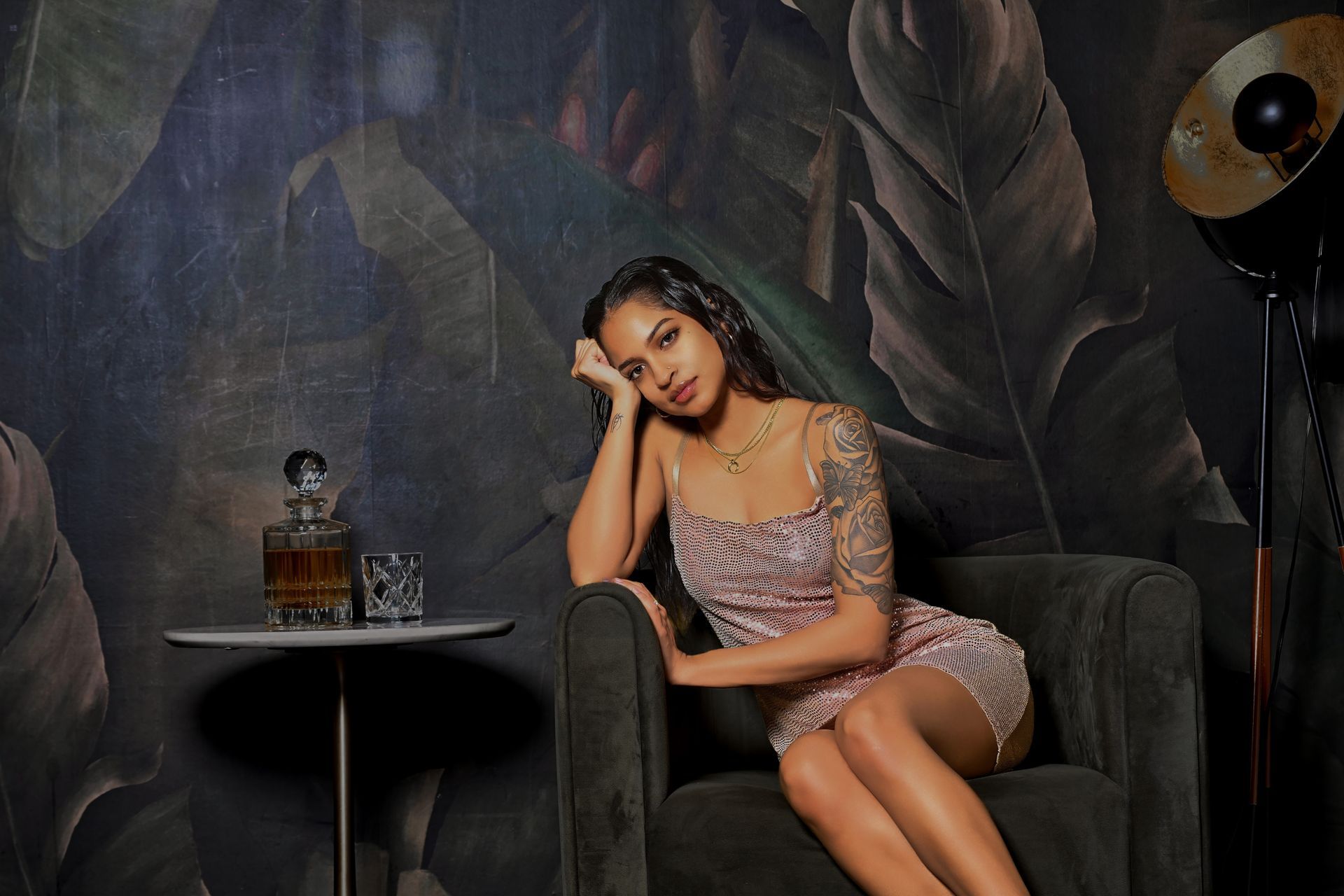 Woman posing on a velvet chair beside a small table in a dim, moody lounge