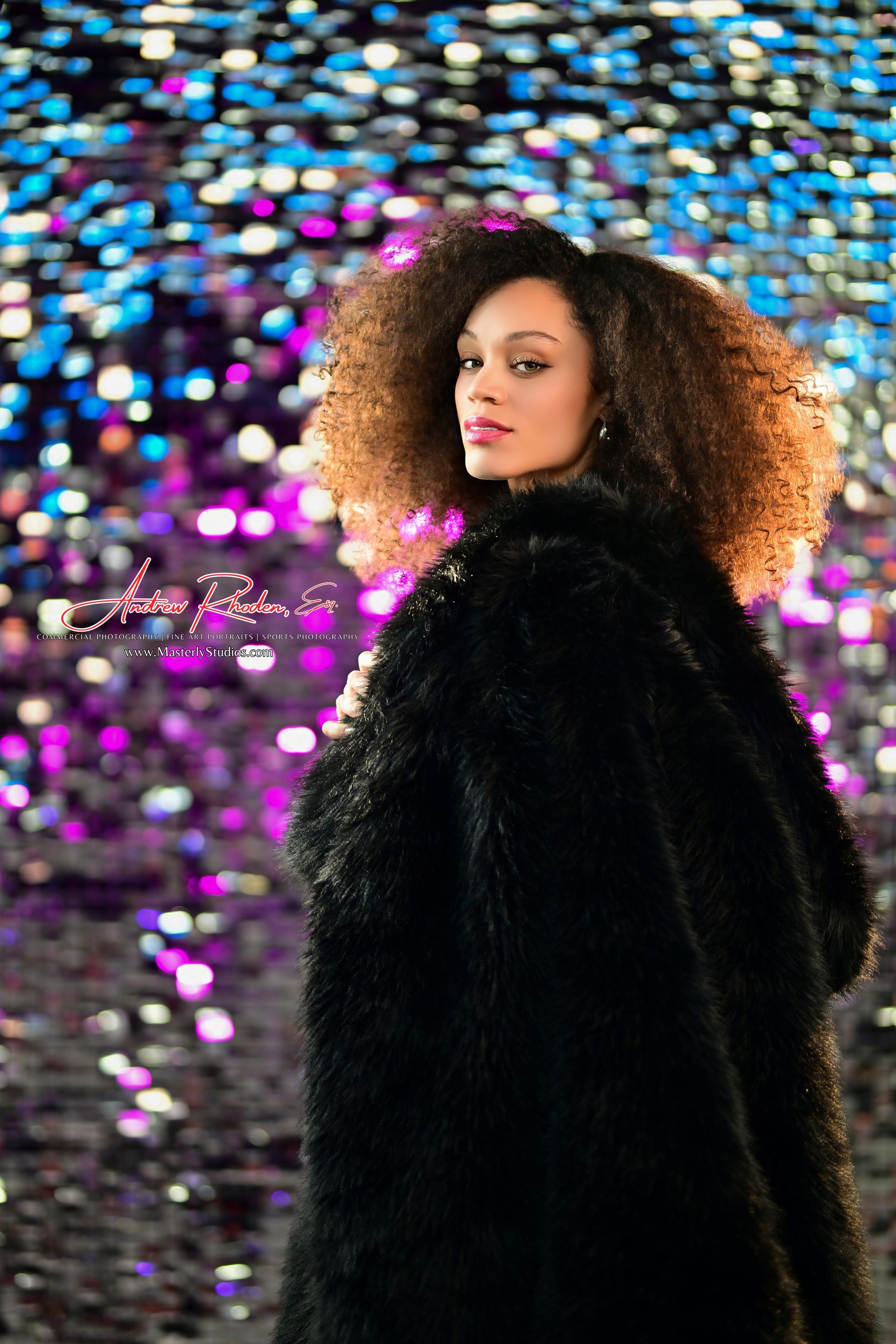 Person in a black coat against a colorful bokeh background, looking over their shoulder.