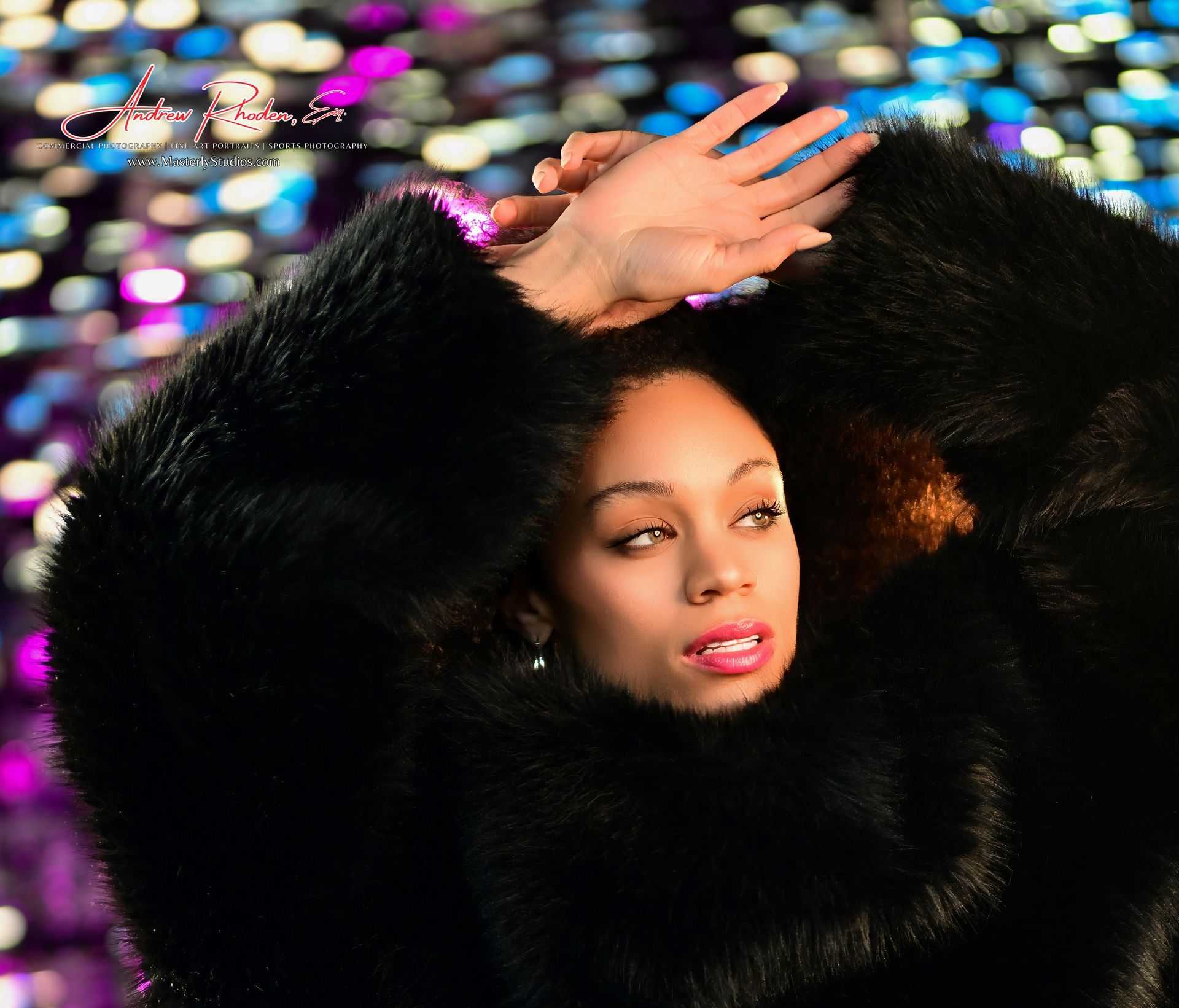 Woman in a black fur coat posing against colorful blurred lights, hand raised over her head