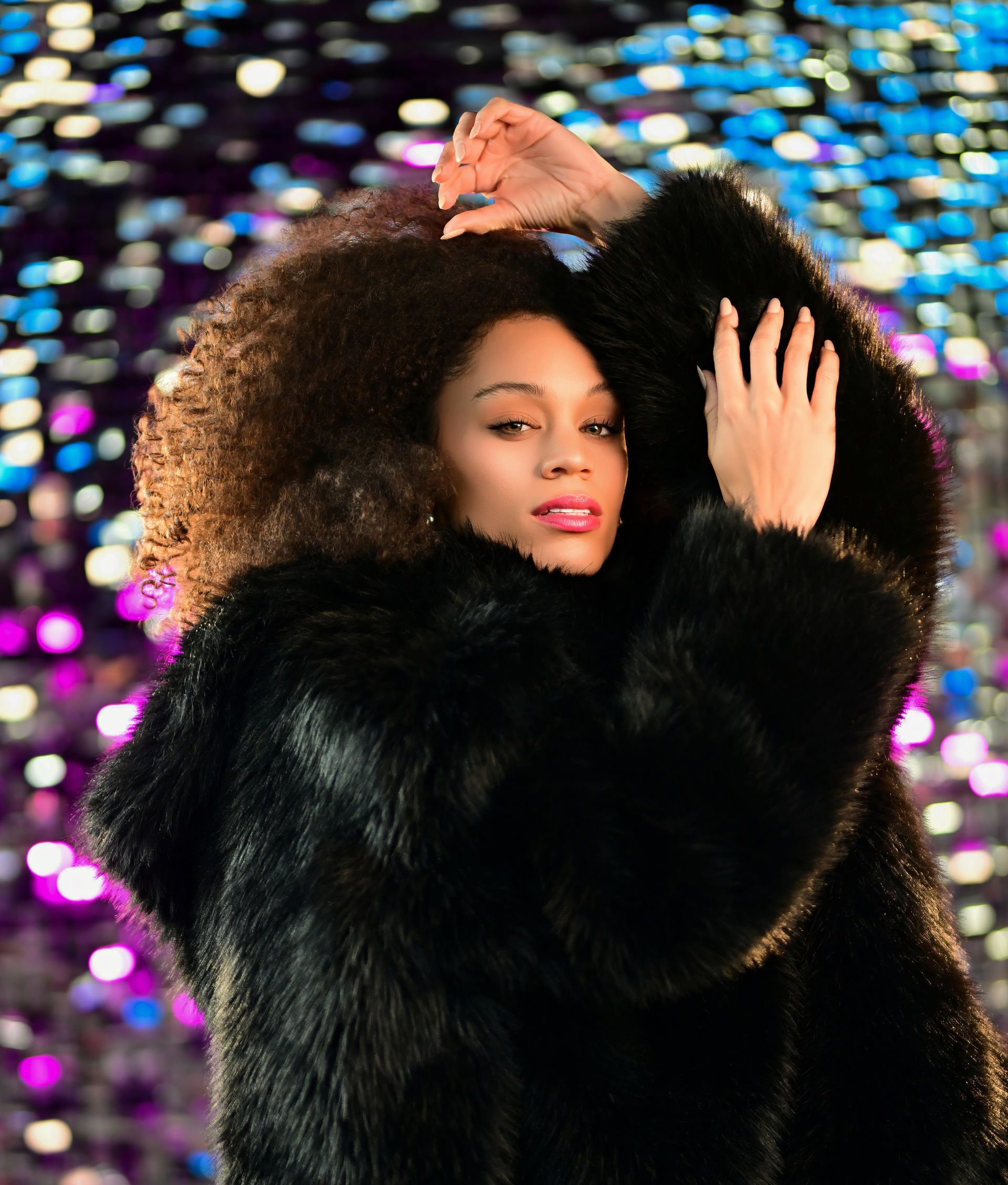 Person in a black fur coat posing against a colorful blurred background.