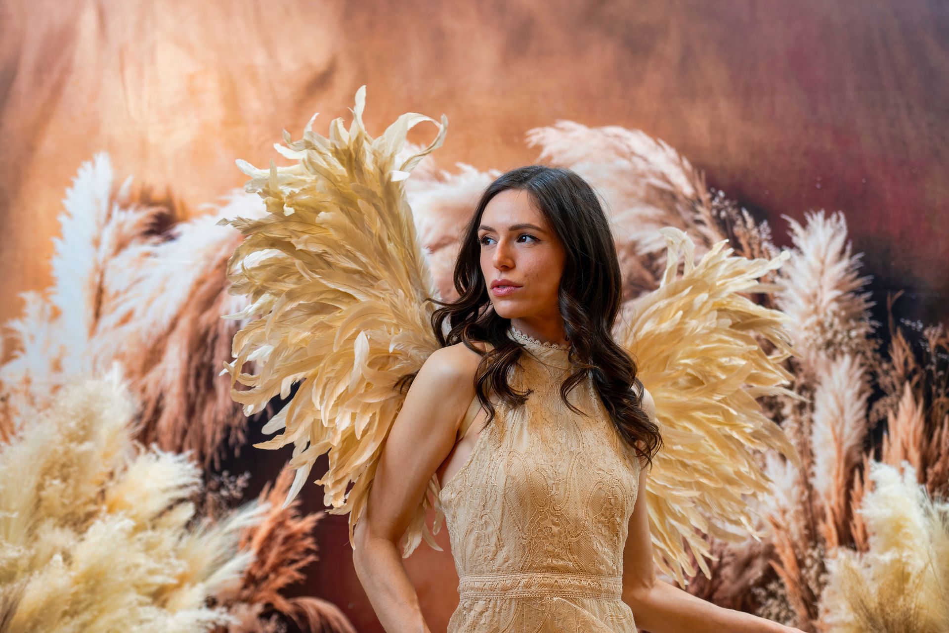 Woman in a gold dress surrounded by large gold feathers against a warm orange backdrop