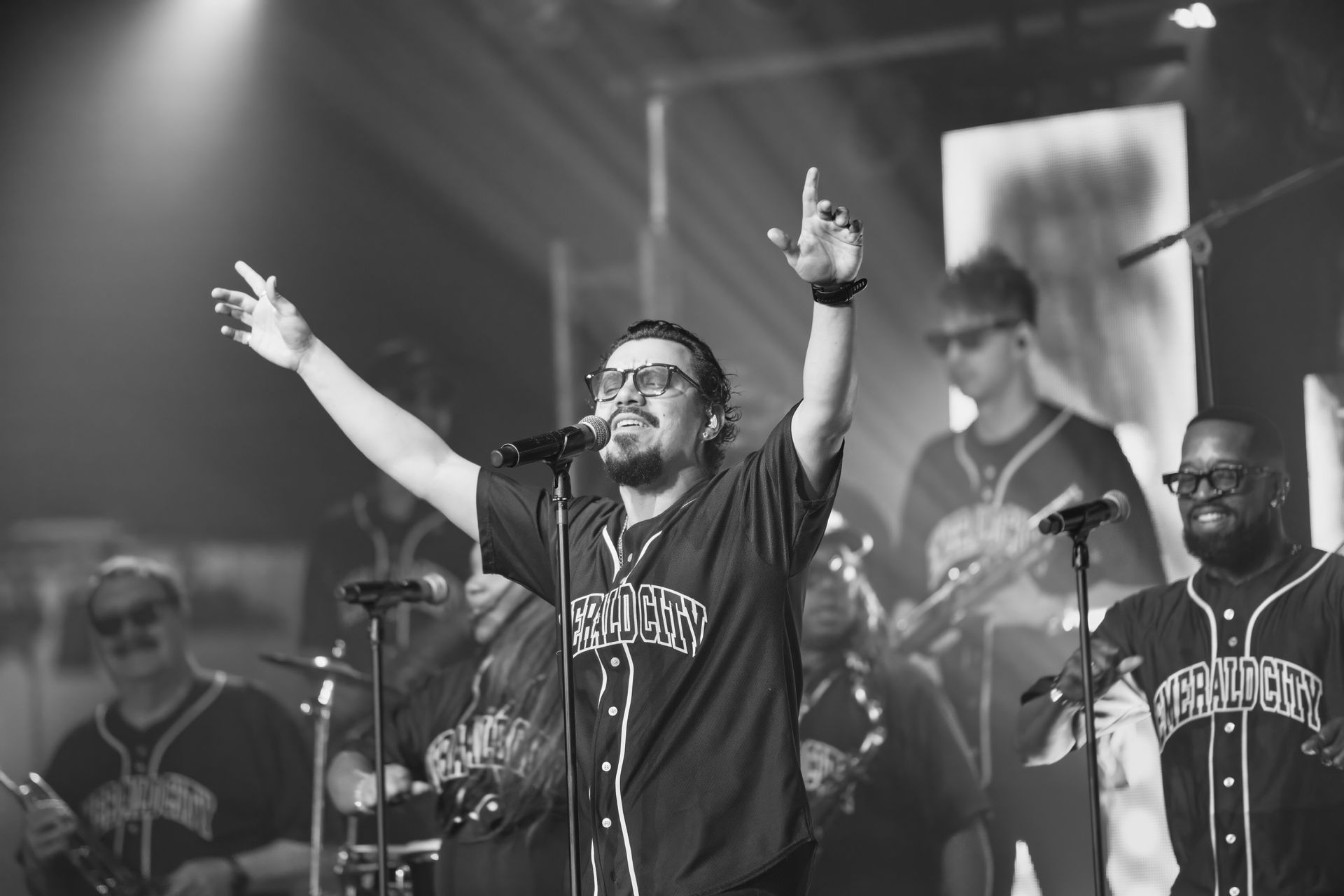 Singer with arms raised on stage, performing with band under bright concert lights