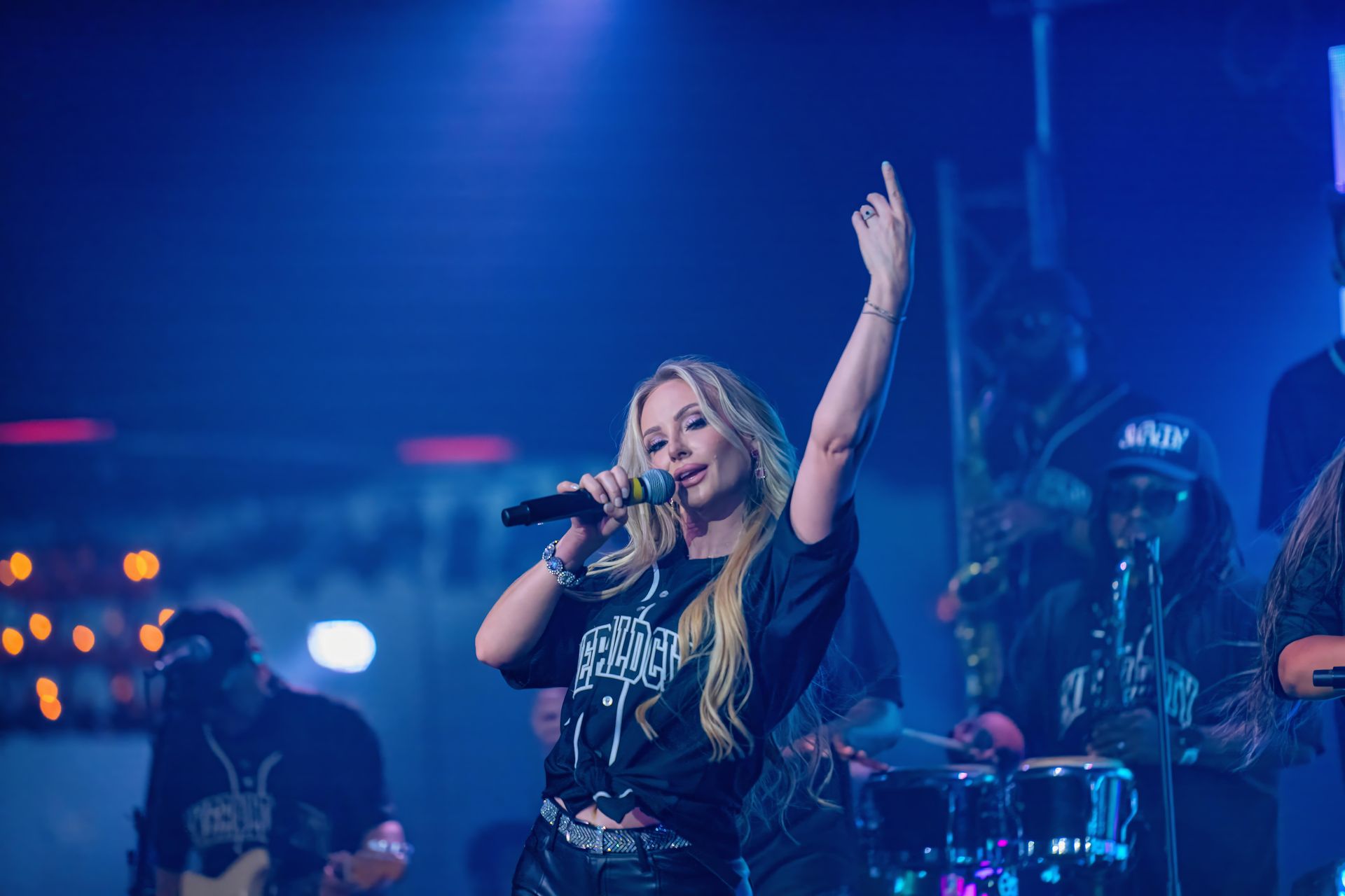 Female singer on blue-lit stage, holding a microphone and raising one arm during a live performance.