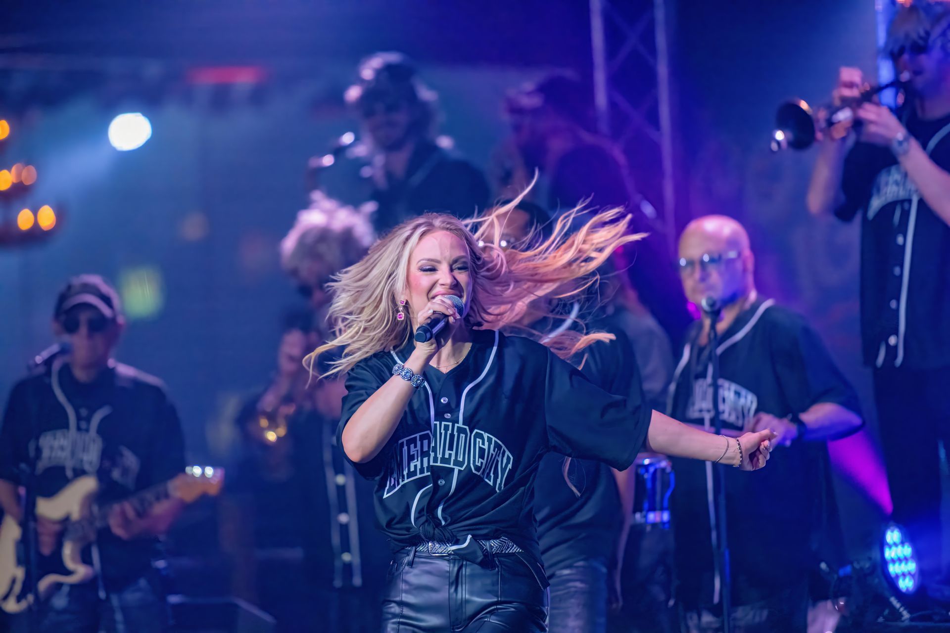 Rock band performing on a purple-lit stage, lead singer singing into a microphone.