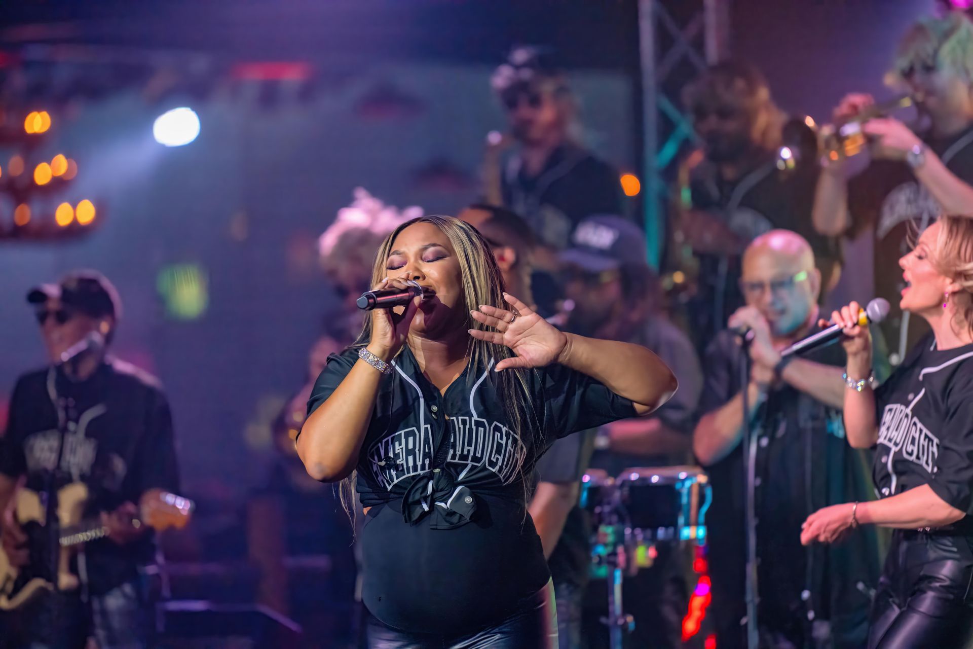 Singer performing on stage with backup musicians and colorful concert lighting