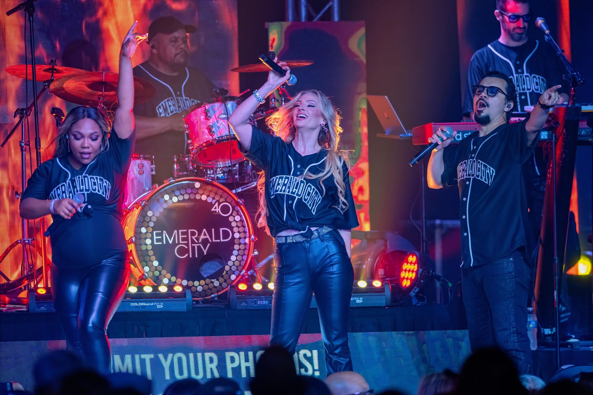 Live band performing onstage under red and blue lights, with singers and drums at Emerald City festival