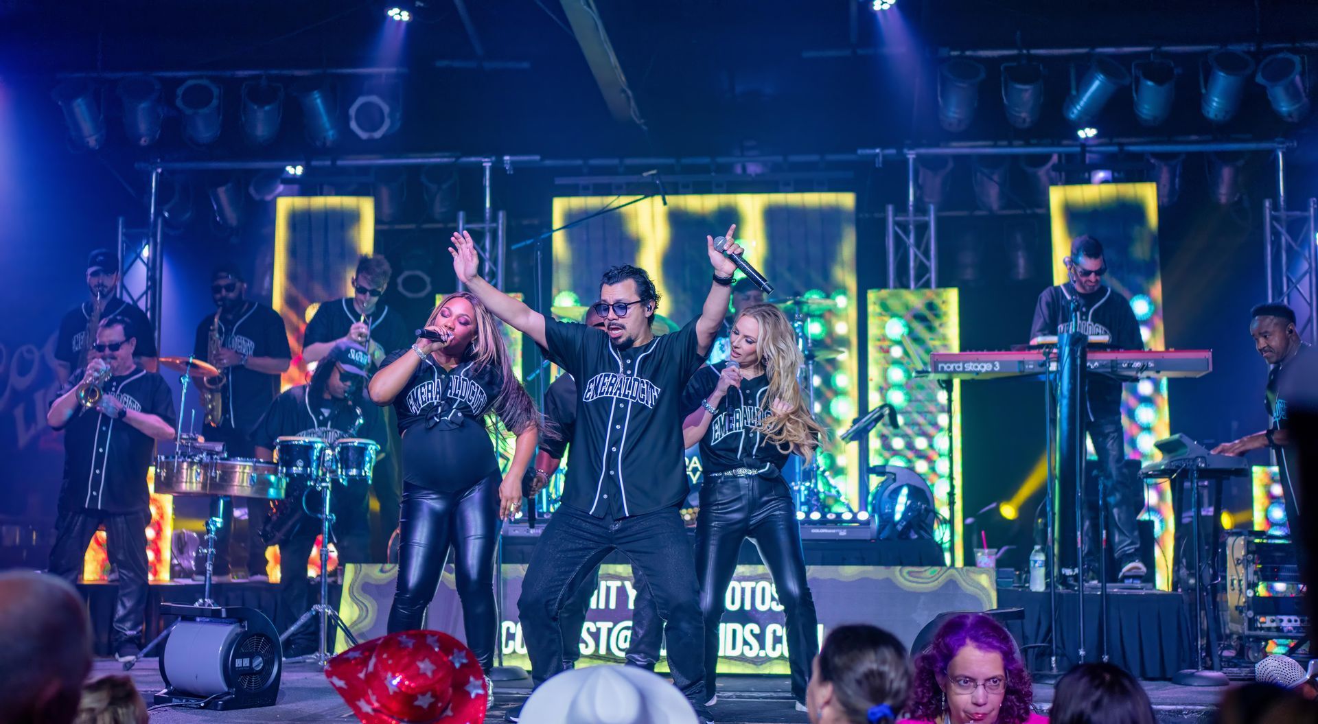 Live band performing on a neon-lit stage, with singer centered and musicians playing around him.