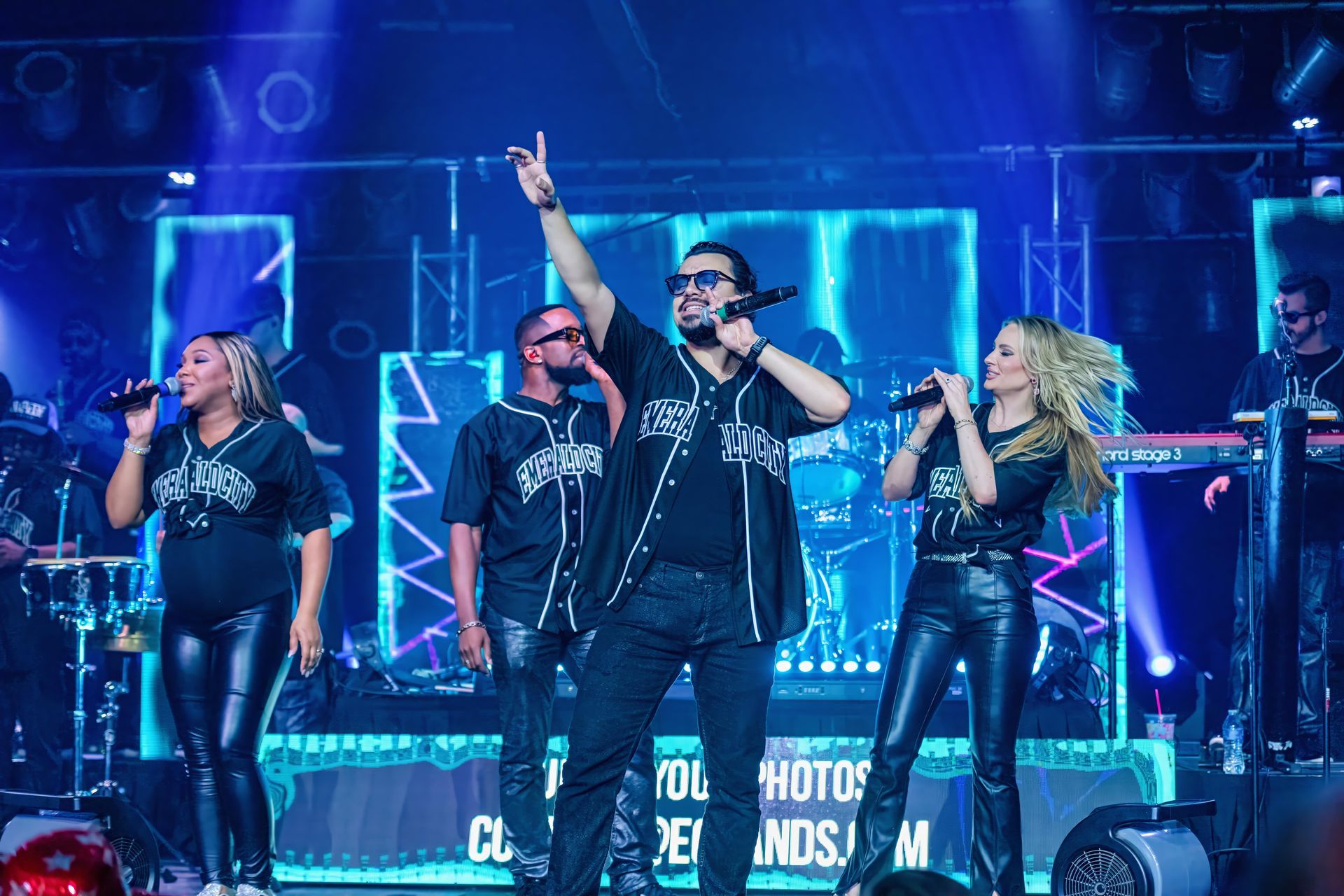 Band performing on a blue-lit stage, with a singer raising one arm and others playing instruments