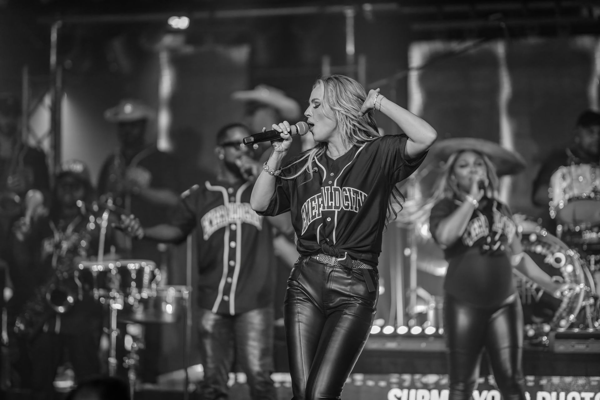 Black-and-white concert performance with a singer holding a microphone center stage, band in the background