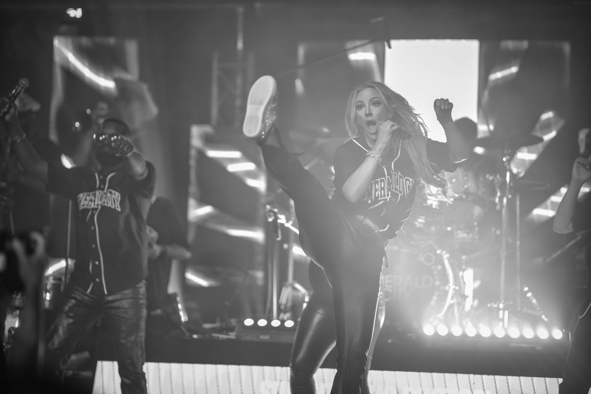 Singer performing on a brightly lit stage with dancers and spotlights in the background