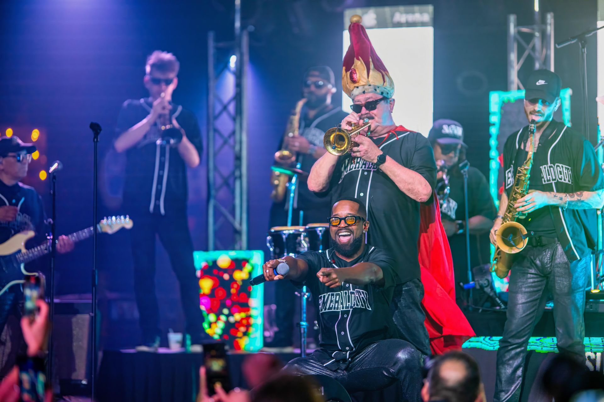Band performing on a colorful concert stage, with a singer in a red cape front and center