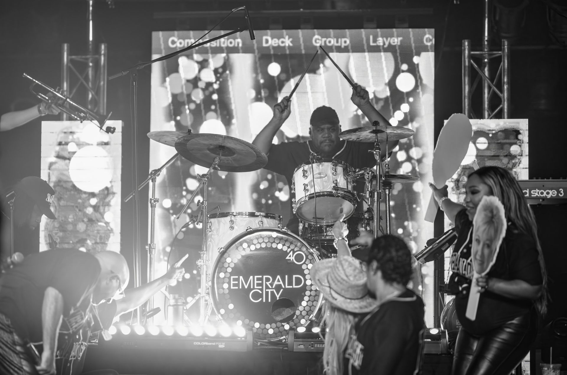 Live band performing on stage with drums and lights, “EMERALD CITY” sign visible in front