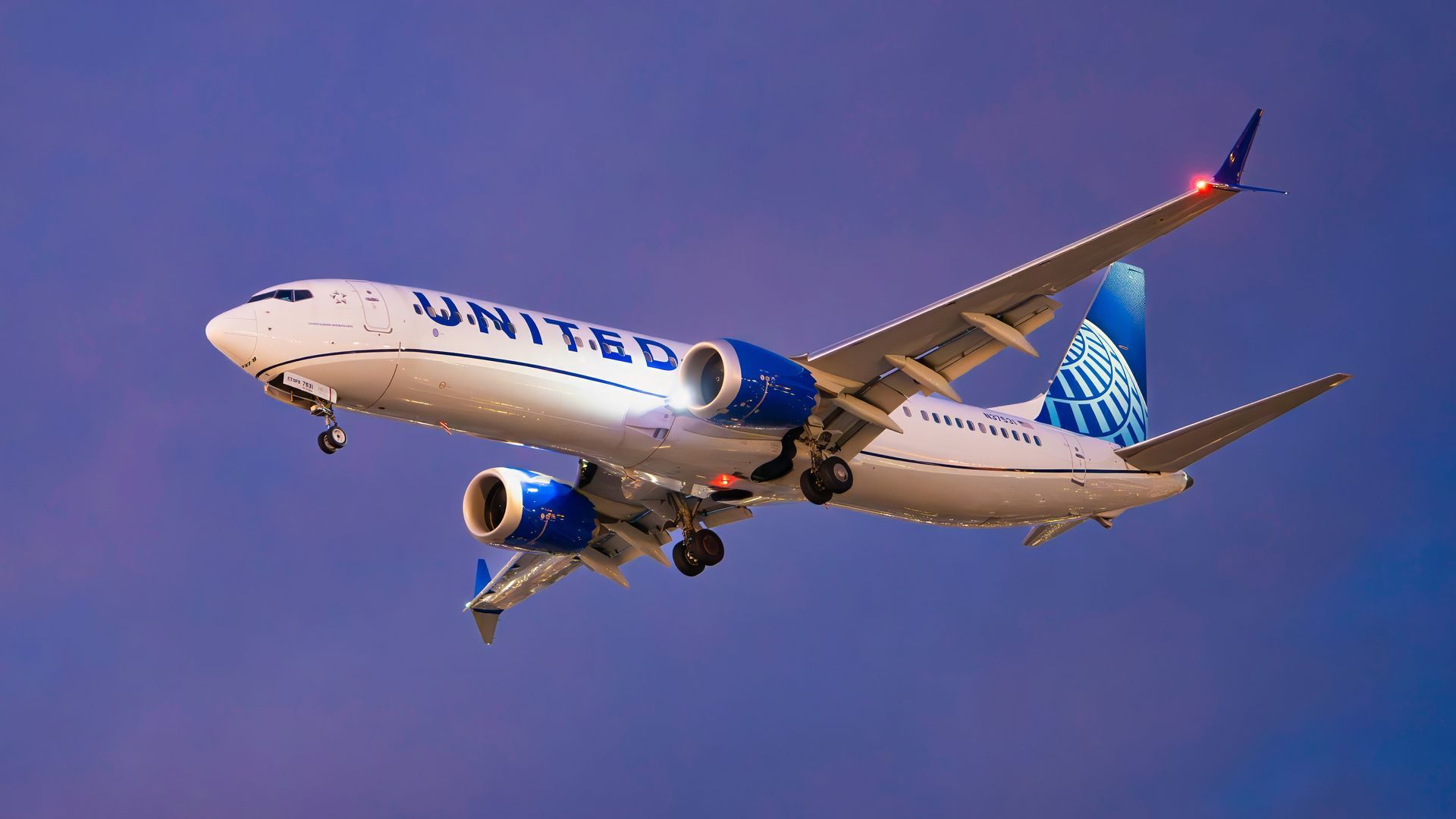 United Airlines jet flying against a purple sky, landing gear down