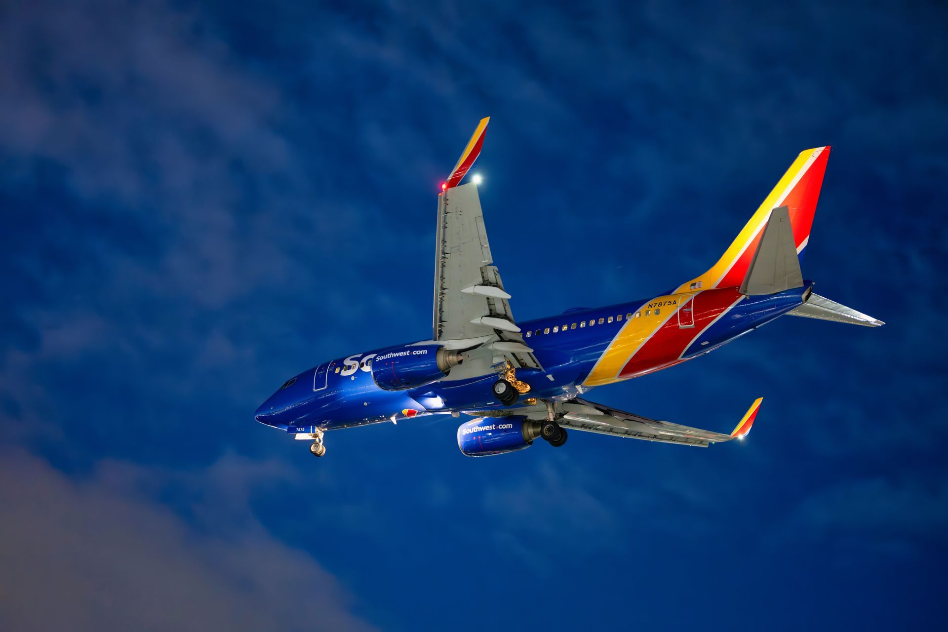 Blue jet aircraft with red-and-yellow tail flying against a cloudy sky