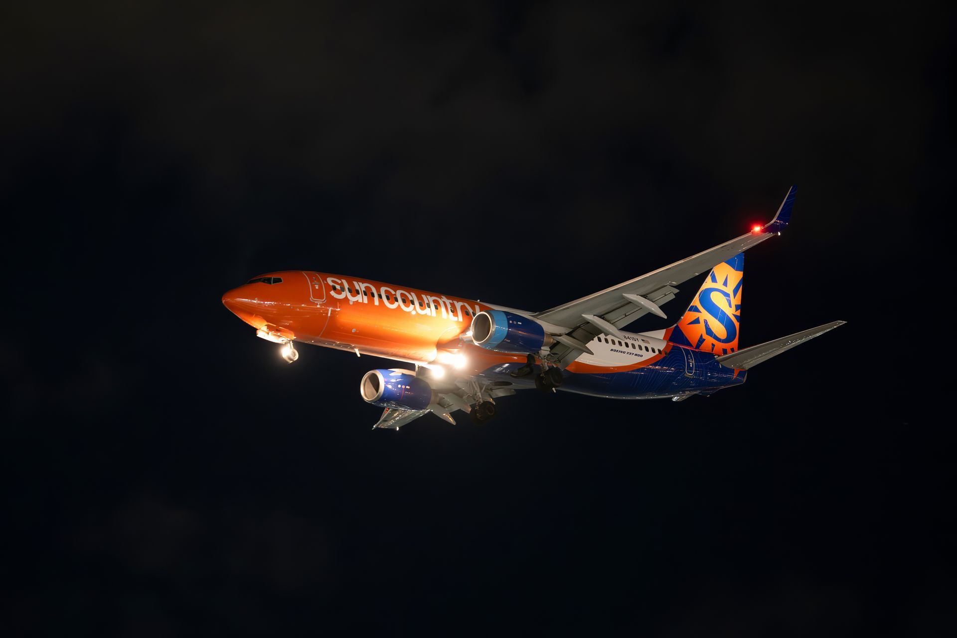 Orange and blue commercial airplane flying at night against a dark sky
