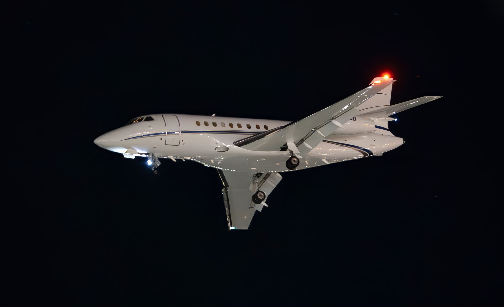 Small jet aircraft flying at night with landing lights on against a dark sky