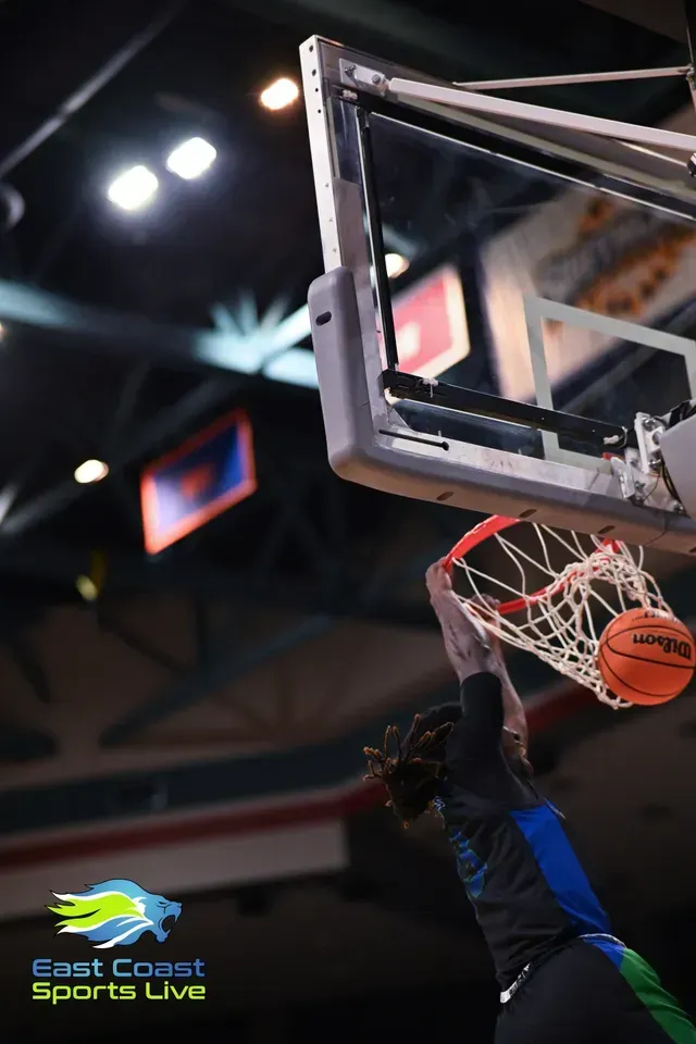 Basketball player dunking near the hoop during an indoor game, orange ball at the rim